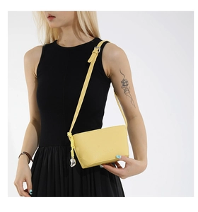 Detail of yellow crossbody bucket bag featuring a silver heart pendant and fashion stamp