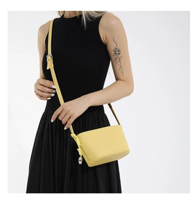 Detail of yellow pebbled leather crossbody bag with adjustable silver buckle and knot charm