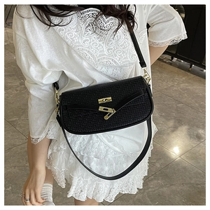 Detail of black woven texture shoulder bag with golden twist lock on white lace outfit