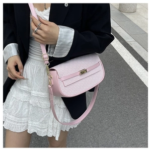 Outdoor street style view of a pink woven crossbody bag with golden metal twist lock