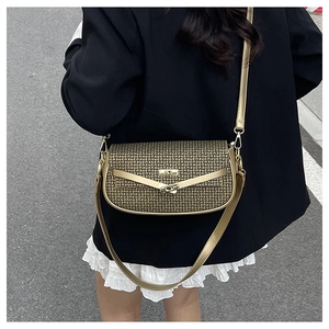 Outdoor street view of a small bronze crossbody bag with textured logo pattern and lock
