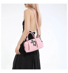 Bolso tipo almohada de cuero rosa con cruz gótica de metal, mostrado en una modelo