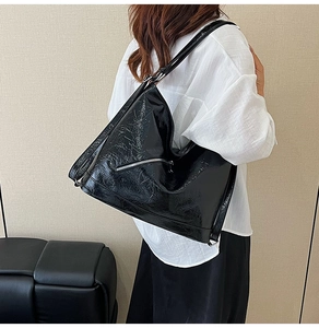 Detail of glossy black leather tote bag with silver zipper and slim shoulder strap