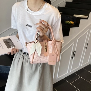 Pink woven bucket bag with golden lock and silk scarf detail held by model