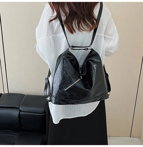 Detail of crinkled black patent leather backpack with diagonal zipper and silver hardware