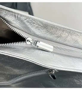Detailed macro view of the smooth silver zipper and metallic crinkled texture on the tote bag