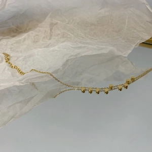 Collana minimalista dorata con piccoli dischi Galaxy e catena sottile su carta bianca