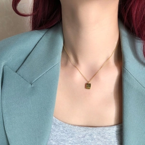 Nahaufnahme einer 14k vergoldeten Halskette mit eckigem Good Luck Anhänger am Model