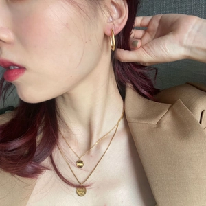 Detail of gold geometric earrings and layered necklace with Good Luck engraving on model