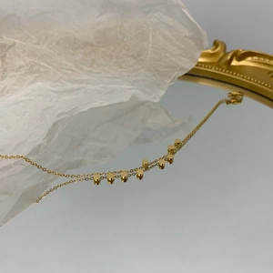 Elegante bracciale a doppia catena dorata con piccoli ciondoli cilindrici su specchio