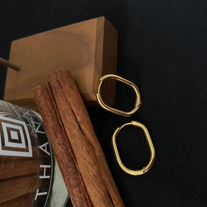 Detailed close-up of golden oval geometric earrings on a textured dark fabric backdrop