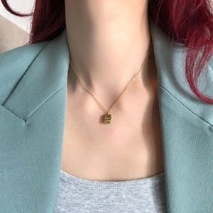Detail einer 14k vergoldeten Halskette mit quadratischem Good Luck Anhänger am Hals getragen