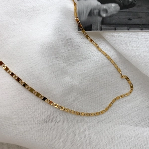 Dettaglio di una collana a maglie dorate su sfondo di lino bianco con texture fine