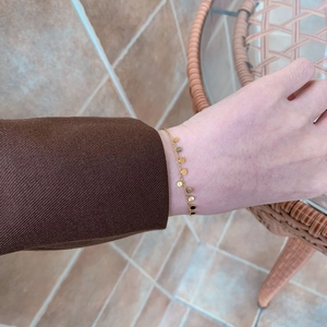 Dettaglio di un bracciale dorato con ciondoli a disco tondo indossato su un maglione