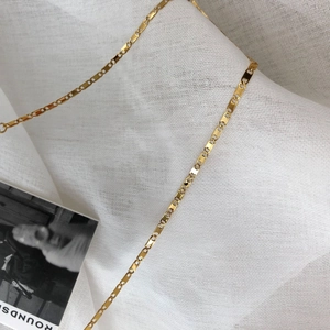 Dettaglio di una catena piatta dorata con maglie rettangolari su un tessuto bianco elegante