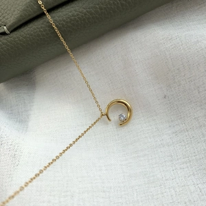 Macro view of gold crescent moon pendant with a sparkling zircon on a dainty chain