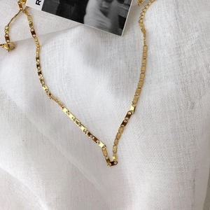 Collana a catena a maglie rettangolari placcata oro 14k su uno sfondo bianco testurizzato