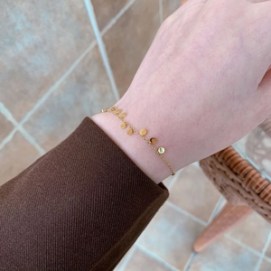Dettaglio di un bracciale minimalista in oro con piccoli dischi lucidi su un polso