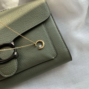 Macro detail of gold moon necklace pendant resting on a textured leather handbag