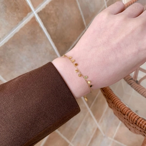 Dettaglio di un bracciale dorato con piccoli ciondoli a disco lucidi su un polso