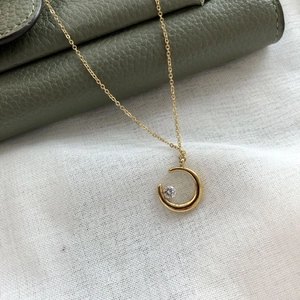 Minimalist gold moon necklace with zircon stone on green leather and white linen fabric
