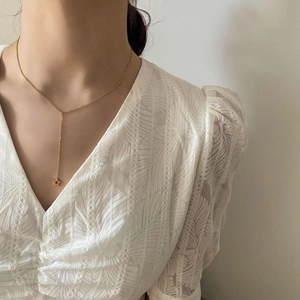 Détail d'un collier en Y doré avec étoile de mer porté par une femme en dentelle