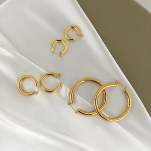 Three pairs of polished gold C-shape hoop earrings in various sizes on white satin