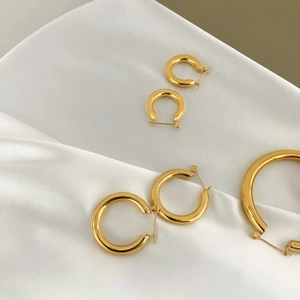 Detailed view of three sizes of thick gold hoop earrings on elegant white silk fabric