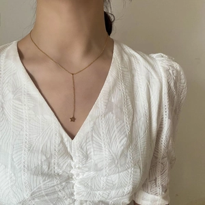 Détail d'un collier en Y doré avec pendentif étoile de mer porté sur un haut en dentelle