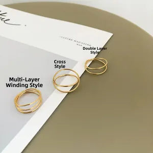 Three gold layered rings with crisscross designs on a white magazine and grey-green background