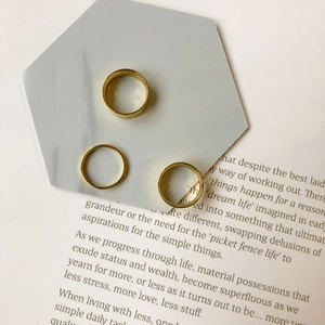 Close-up of three polished gold stackable rings in various widths on marble background