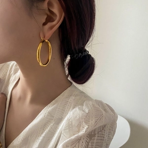Close-up of a large polished gold hoop earring worn by a model in a side-view shot
