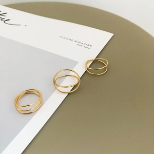 Three-piece set of gold minimalist layered cross-wrapped rings on a white magazine background