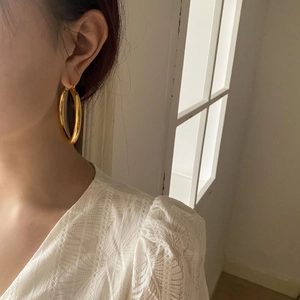 Close-up of model wearing large polished gold hoop earrings with minimalist metal design