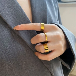 Close-up of a three-piece gold minimalist wide ring set worn against a grey blazer
