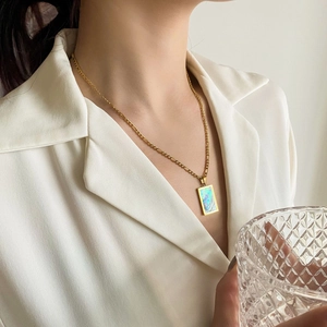 Dettaglio di un ciondolo rettangolare turchese su catena d'oro indossato da una donna in bianco
