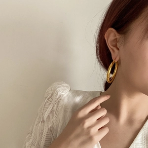 Close-up of a model wearing large polished gold hoop earrings in minimalist style