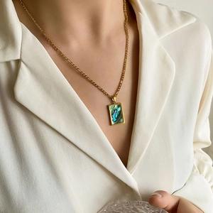 Dettaglio di una collana dorata con ciondolo rettangolare in madreperla su camicia bianca