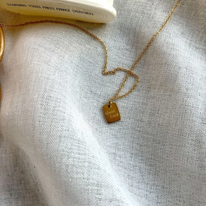 Vergoldete 14k Halskette mit rechteckigem 'Good Luck' Anhänger auf weißem Leinenhintergrund