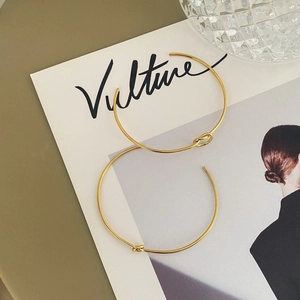 Minimalist gold knot cuff bracelet with curved open design on a lifestyle background