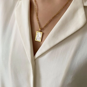 Dettaglio di una collana a catena Figaro dorata con pendente rettangolare in conchiglia