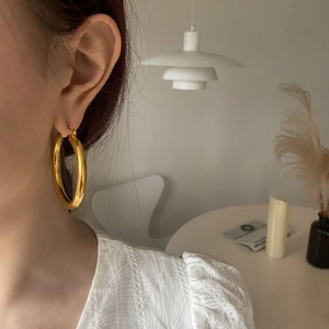 Detail of large high-polish gold hoop earring worn by a model in a warm lifestyle setting