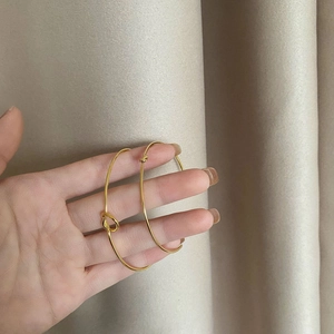 Minimalist gold-plated knot cuff bracelets displayed on a warm textured background