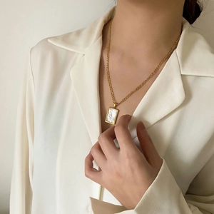 Dettaglio della collana d'oro con pendente in madreperla bianca su una camicia di seta