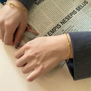 Detail of minimalist gold knotted bangles worn on wrist against a vintage background