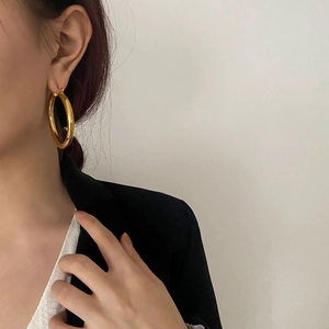 Detailed view of large polished gold hoop earrings worn with a black blazer