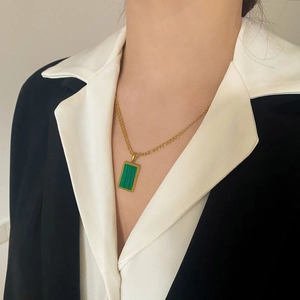 Dettaglio di una collana dorata minimalista con un pendente rettangolare in malachite su modella