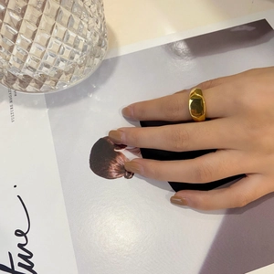 Nahaufnahme eines breiten polierten Gold-Titanrings mit unregelmäßigen Facetten
