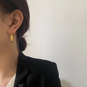 Close-up of a polished gold teardrop hoop earring worn by a model in black attire