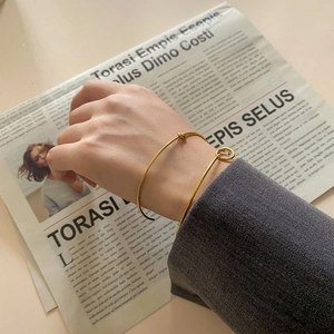 Minimalist gold knot open cuff bracelet set styled on wrist with gray blazer suit